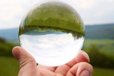 Close-up of hand holding crystal ball against sky