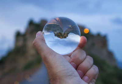 Cropped image of man hand holding crystal ball against mountain