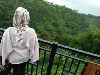 Rear view of woman looking at forest while standing by railing