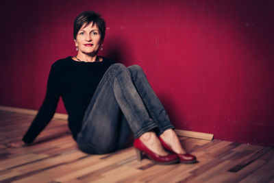 Portrait of young woman sitting on floor against wall