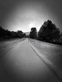 Empty road by trees against sky in city