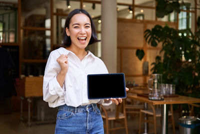 Portrait of smiling young woman using digital tablet while standing in cafe