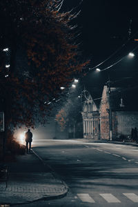 Man walking on illuminated street in city at night