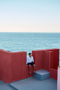 Young latin man meditative in a red building, sea on background