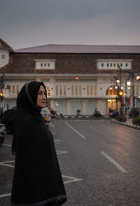 Woman standing on road against buildings in city