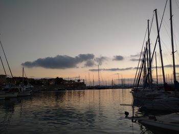 Sailboats moored at harbor against sky during sunset