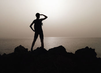 Silhouette woman standing on rock by sea against clear sky