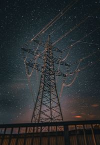Low angle view of electricity pylon against sky at night