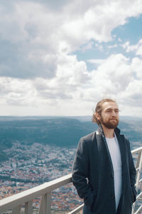 Young man looking at city against sky