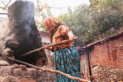 Low angle view of woman putting wood in oven