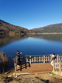 Man standing on lake against clear blue sky