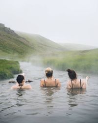 Rear view of people enjoying in water against sky