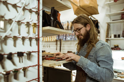 Smiling shoemaker looking at tools in workshop