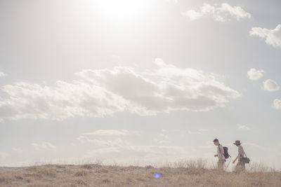 Side view of friends walking on field against sky