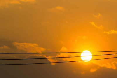 Low angle view of power lines against orange sky