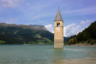 Lighthouse by sea and buildings against sky