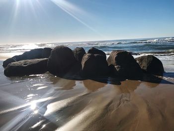 Rocks on beach against sky on sunny day