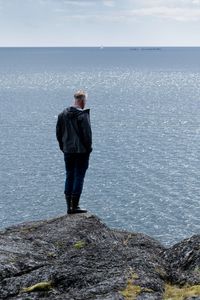 Man standing on rock looking at sea shore against sky