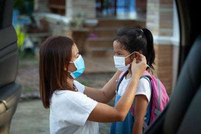 Side view of mother wearing flu mask to daughter outdoors