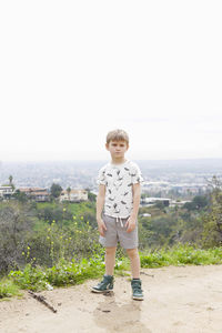Full length portrait of boy standing on field against sky
