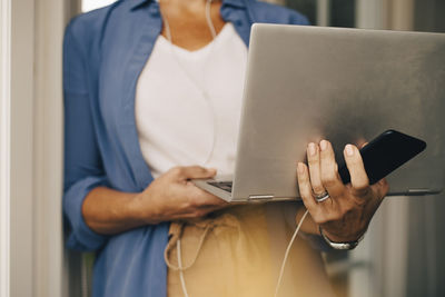 Midsection of woman holding laptop and smart phone at holiday villa