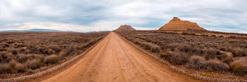 Panoramic shot of dirt road amidst land against sky