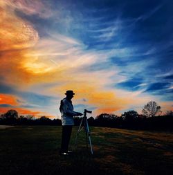 Man photographing on field against sky during sunset