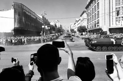 Group of people photographing in city against sky
