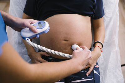 Female nurse examining pregnant woman abdomen by ultrasound baby heartbeat monitor