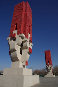 Low angle view of sculpture against building against clear blue sky