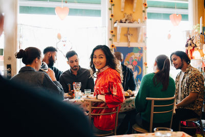 Portrait of smiling young woman sitting amidst multi-ethnic friends during brunch party in restaurant