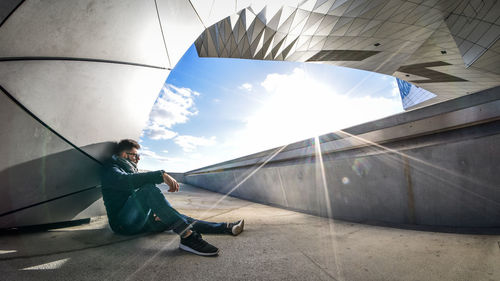 Side view of young man sitting against sky