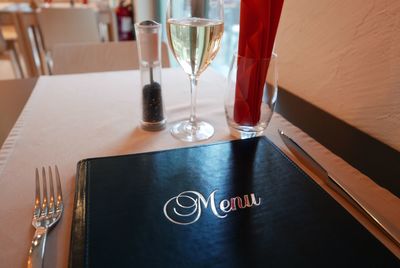 Menu by pepper shaker and white wine on table in restaurant