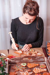 Woman decorating christmas gingerbread cookies at home