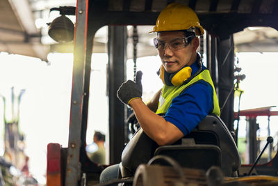 Engineer or technician concept. a male employee driving a forklift and showing thumb up in factory.