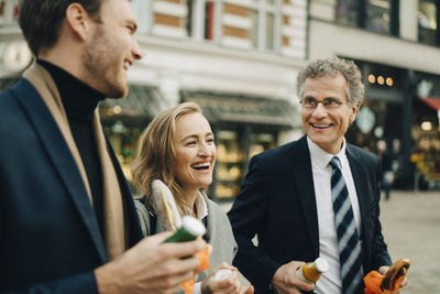 Smiling business colleagues discussing while holding food and drink in city