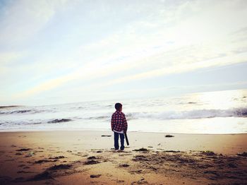 Rear view of boy on beach against sky