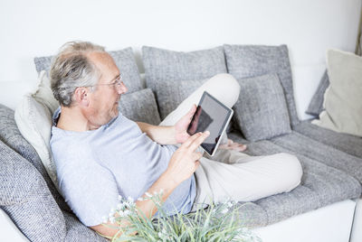 Mature man at home lying on couch using digital tablet