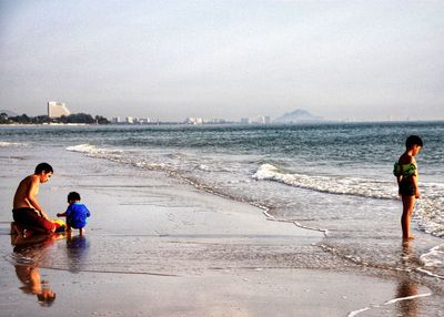 Father with sons at beach against sky