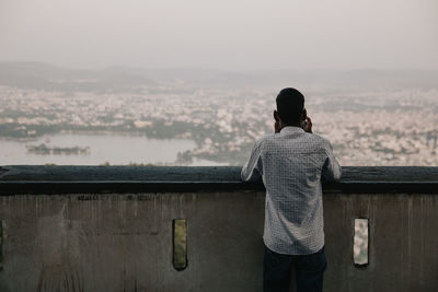 Rear view of man looking at a city against sky
