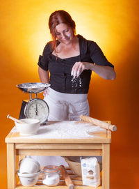 Woman preparing food standing by orange background