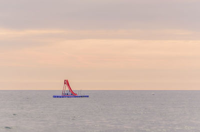 Slide on diving platform in sea against sky during sunset