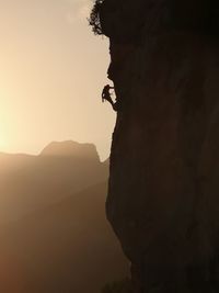 Side view of silhouette man on rock at sunset