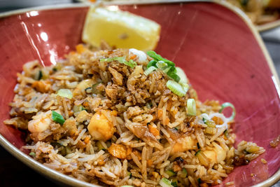 A tasty bowl of oriental style prawn fried rice served with a lemon wedge close up