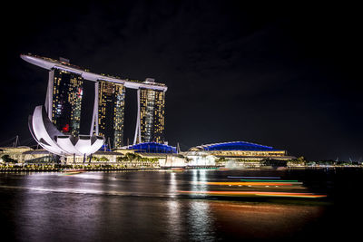 Illuminated city by river against sky at night