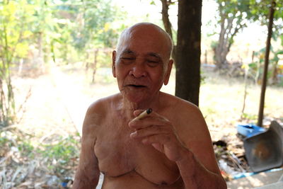 Shirtless senior man smoking cigarette while sitting outdoors