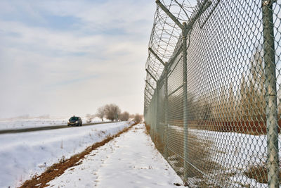 Snow covered fence by trees against sky