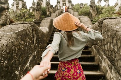 Close-up of man holding hand of woman wearing hat on staircase