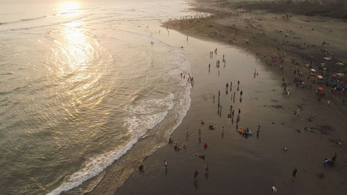 Sandy beach parangtritis near ocean with big waves, people in tropical resort at sunset. yogyakarta