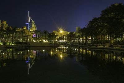 Low angle view of illuminated burj al arab in front of river at night in city